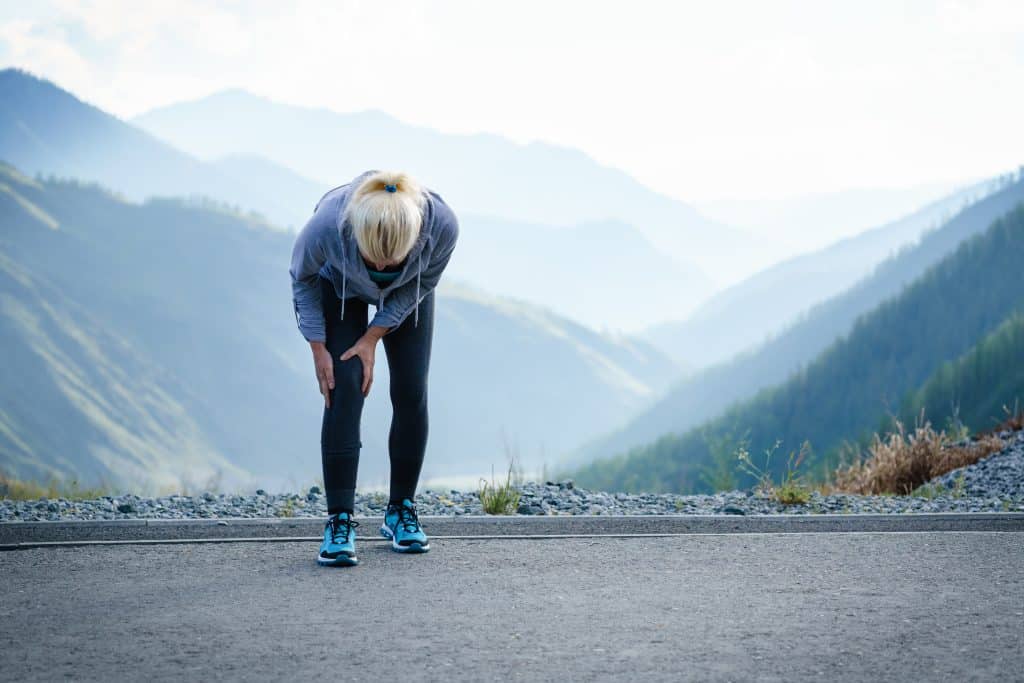 A runner leans down, holding her knee, which seems to be hurt