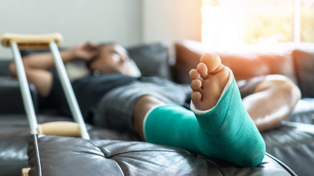 Bone fracture foot and leg on male patient with splint cast and crutches during surgery rehabilitation and orthopedic recovery staying at home