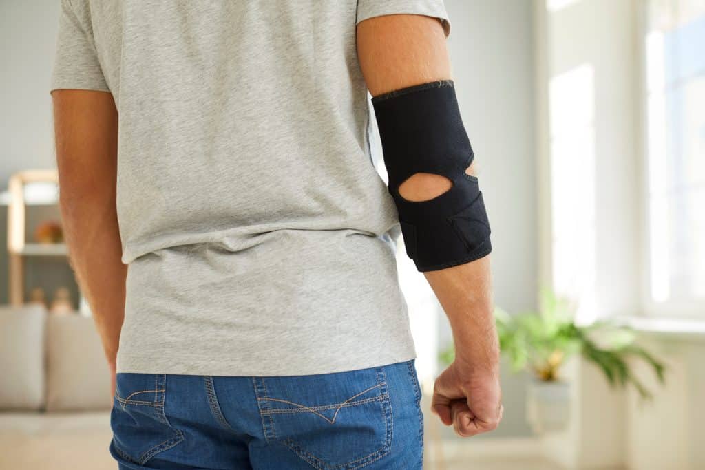 Young man wearing an adjustable black neoprene orthopedic elbow support brace for easing pain in the elbow