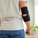 Young man wearing an adjustable black neoprene orthopedic elbow support brace for easing pain in the elbow