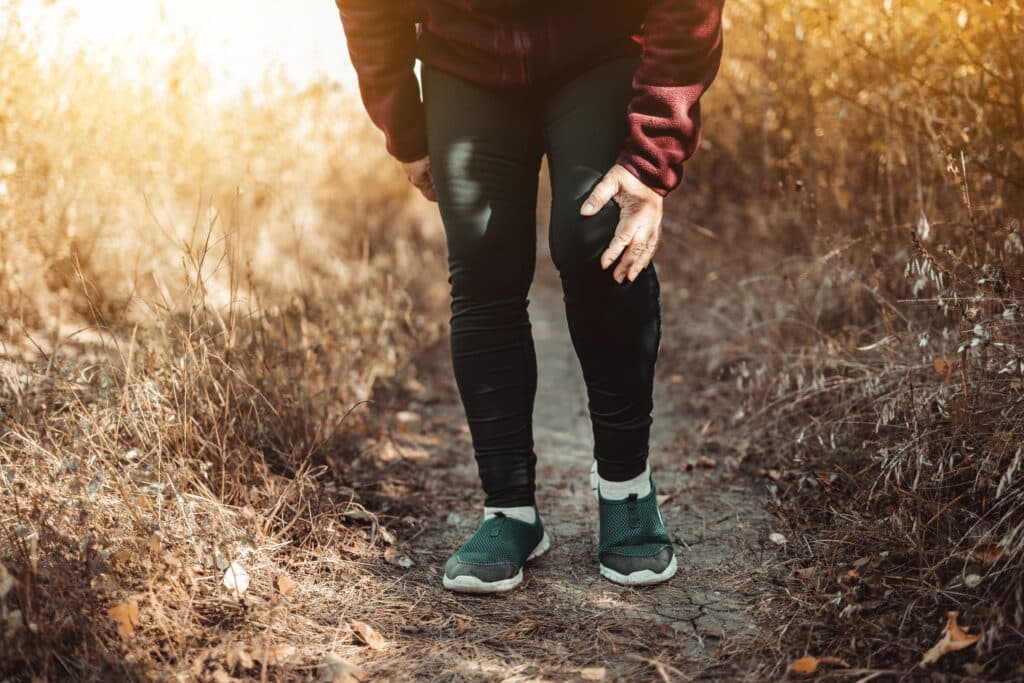 Female athlete with osteoarthritis holding her knee in pain during a run