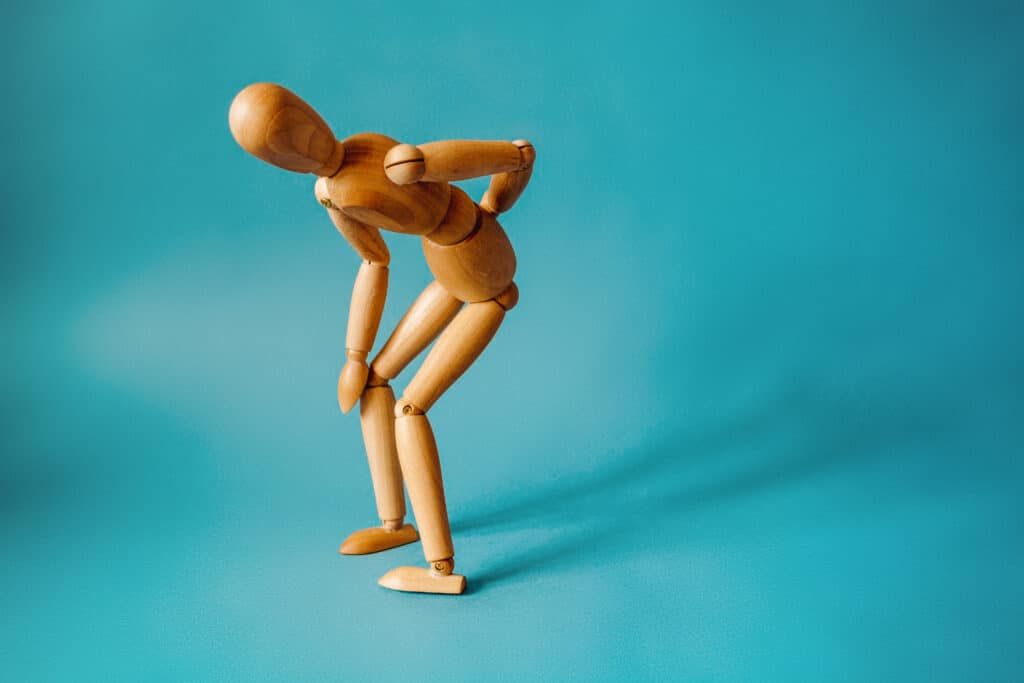 A wooden figure bent over and holding their back to illustrate back and spine pain.