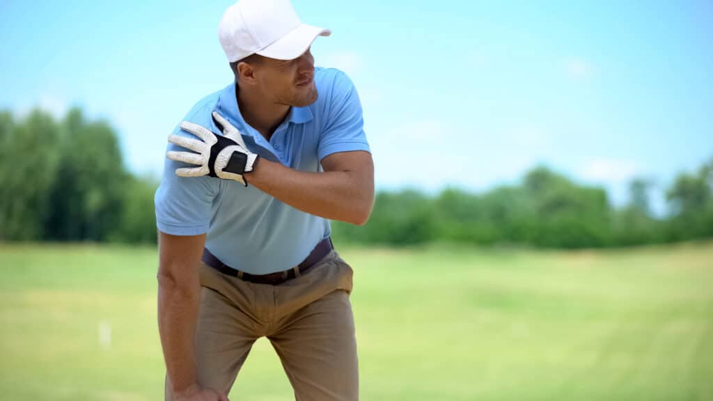 A golfer grabbing his shoulder in pain, which is caused by a bone spur in the shoulder.