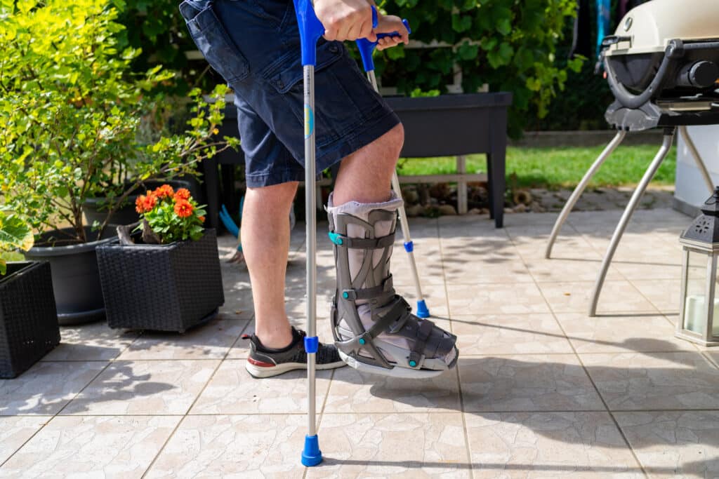 A person wearing a walking boot and using hand crutches due to a fractured fibula.