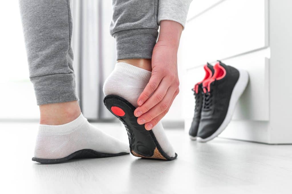 A person trying on orthopedic insoles to treat pronation or supination with running shoes in the background.