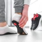 A person trying on orthopedic insoles to treat pronation or supination with running shoes in the background.